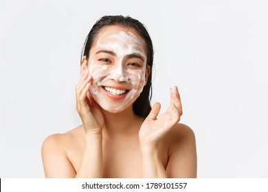 Skincare, women beauty, hygiene and personal care concept. Close-up of happy smiling asian woman standing naked in bath, using daily-care skin cleansing foam and looking delighted, white background