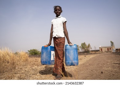 Skinny African Girl Carrying Two Water Containers In The Middle Of An Arid Landscape; Concept Of Poverty, Lack Of Pipe Connections In Private Rural Homes, Child Labor; Millennium Development Goals