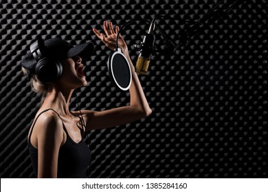 Skinny Blonde Hair Asian Adult Woman With Cap Earphone Sing A Song Loudly With Power Sound Over Microphone Condenser Filter In Black Shirt. Egg Studio Lighting Shadow Crate Sound Absorbing Wall Room