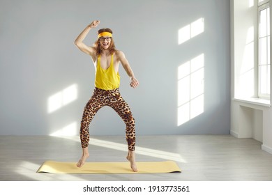 Skinny fitness nerd having fun during sports workout at home. Funny thin young guy in yellow sweatband and hilarious leopard leggings looking at camera and smiling while dancing and jumping on gym mat