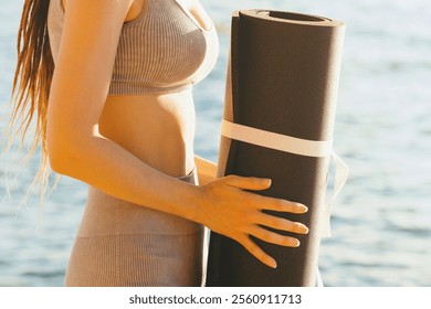 Skinny woman with dreadlocks standing with rolled up yoga mat against sea background. Outdoor workouts, meditation, yoga, body care - Powered by Shutterstock