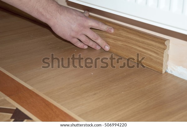 Skirting Board & Architrave. Repairman\'s\
hands Installing Skirting Board Oak Wooden Floor with Glue.\
Flooring and Repair.