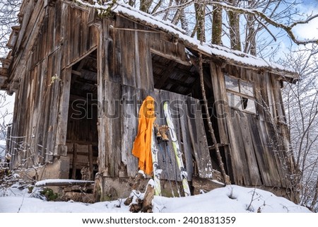 Skis and ski poles leaning against an old, abandoned and dilapidated wooden hut in a romantic snowy landscape in Tyrol