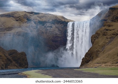 Skogafoss, a famous waterfall in southern Iceland, flows and creates a blanket of mist on an overcast day. - Powered by Shutterstock