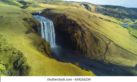 Skogafoss waterfall from aerial view behind green and yellow grass cliff, South Iceland
