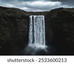 Skogafoss waterfall cascades from a rocky cliff under an overcast sky, captured by drone in Iceland