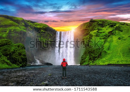 Skogafoss waterfall in Iceland. Guy in red jacket looks at Skogafoss waterfall.