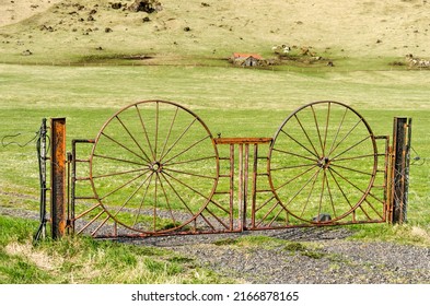 Skogar, Iceland, April 22, 2022: old and rusty fence, with the shape of wheels, in a green landscape with a small farm and cows in the background