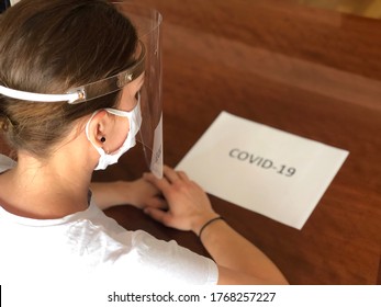 Skopje, Macedonia- July 2,2020: Woman Working Protected With White Medical Mask And Plexiglass Face Shield From Coronavirus Covid-19 And White Paper With Text Covid-19