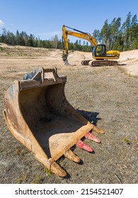Skrunda, Latvia - May 3, 2022: Yellow excavator JCB JS 220 LC and removed rusty excavator bucket is located in a quarry.