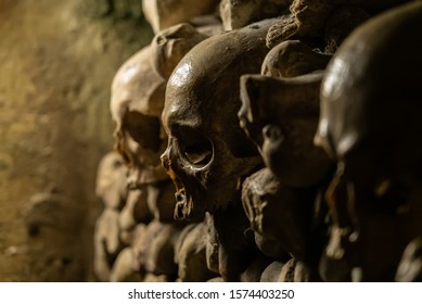 Skulls and bones in catacombs. Old broken skull placed in the wall of bones. Grim lighting. Underground cemetery.