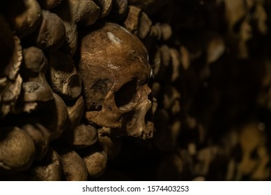 Skulls and bones in catacombs. Old broken skull placed in the wall of bones. Grim lighting. Underground cemetery.