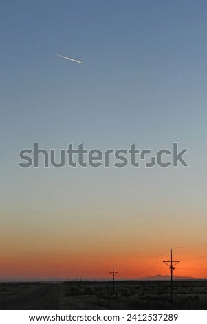 The sky is aflame with the setting sun, casting a golden glow across the open prairie and power lines in the foreground