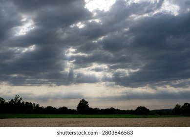 Sky Background. Panoramic view of a cloudscape with sun's rays piercing through storm clouds and countryside with wheat field and trees
