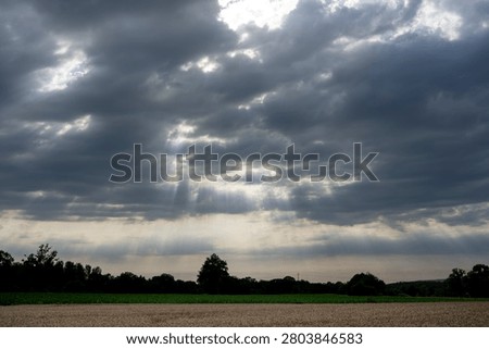 Sky Background. Panoramic view of a cloudscape with sun's rays piercing through storm clouds and countryside with wheat field and trees