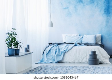 Sky blue bedroom interior with double bed, plants and grey boxes on the floor