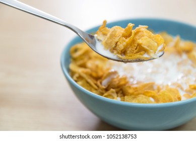 A sky blue colored bowl of delicious corn flake cereals and milk and a spoon with cereal on a wooden surface - Powered by Shutterstock