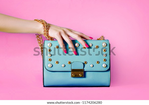 Sky blue handbag purse and\
beautiful woman hand with red manicure isolated on pink\
background.