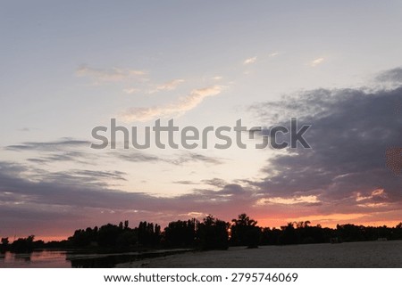 The sky displays a gradient of soft pinks and oranges as clouds drift across the horizon above a calm body of water and a dark treeline