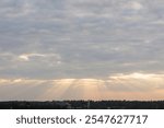 sky filled with clouds during either sunrise or sunset. Sunlight is breaking through the clouds in several places, creating a dramatic effect known as “God rays” or “crepuscular rays.” 