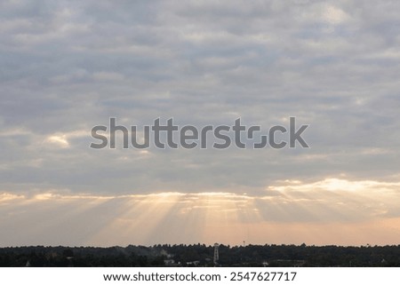 sky filled with clouds during either sunrise or sunset. Sunlight is breaking through the clouds in several places, creating a dramatic effect known as “God rays” or “crepuscular rays.” 