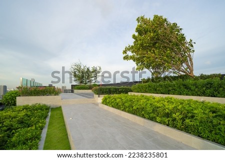 Sky garden on private rooftop of condominium or hotel, high rise architecture building with tree, grass field, and sunset sky.
