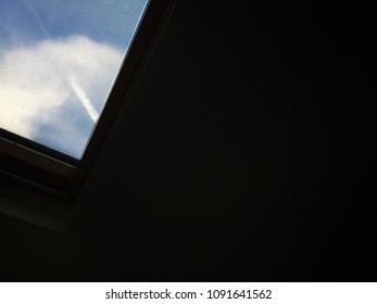 Sky Through Skylight Window. Dark Background With Image On Top Left Of Blue Sky With White Cloud And Vapour Trail Through Lower Right Corner Of A Skylight Window. Space To Write Text