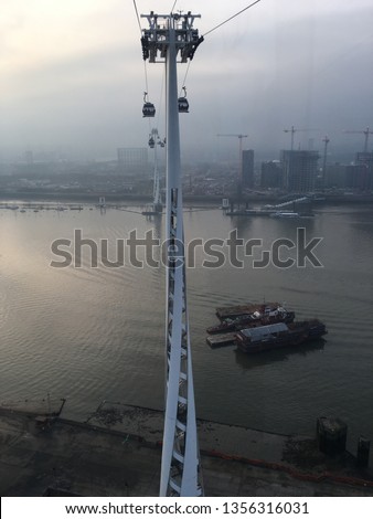 Sky view from London Cable car (Gondola Lift, Dangleway, IFS Cloud) and spiral tower (pylon), across (over) River Thames - transport for London, UK, EU, between Greenwich Peninsula and Royal Victoria.