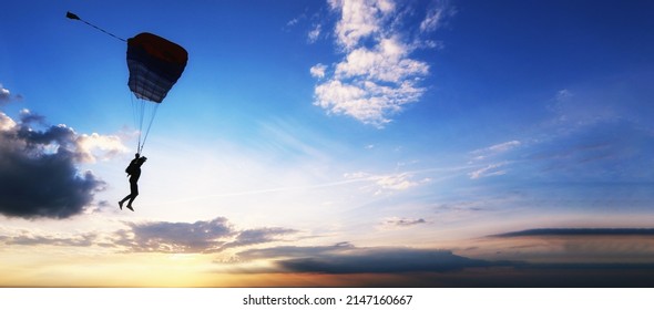 Skydiver is flying on the background of setting sun and clouds.A man on a parachute conquers the sky. Aerodynamics above the river and beautiful landscape.Extreme tourism banner. National airborne day - Powered by Shutterstock