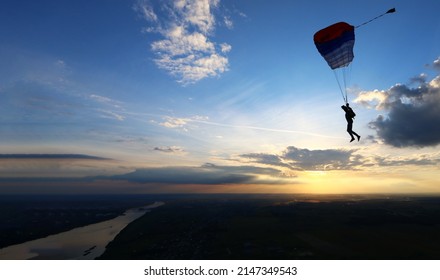 Skydiver is flying on the background of setting sun and clouds.A man on a parachute conquers the sky. Aerodynamics above the river and beautiful landscape.Extreme tourism banner. National airborne day