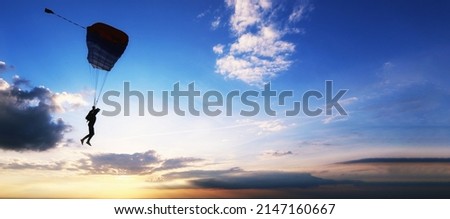 Skydiver is flying on the background of setting sun and clouds.A man on a parachute conquers the sky. Aerodynamics above the river and beautiful landscape.Extreme tourism banner. National airborne day