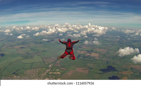 Skydiver in a red jumpsuit freefalling above the clouds