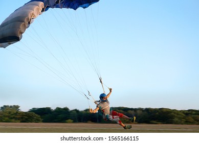 Skydiver under a dark blue little canopy of a parachute is landing on airfield, close-up. High-speed landing of a parachuter against the background of forests and buildings.