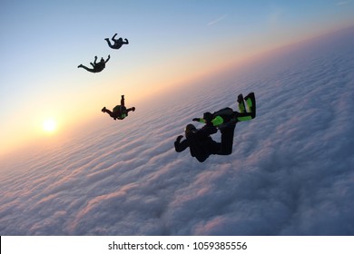 Skydivers are flying above pink clouds.