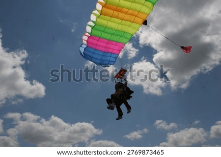 Skydiving – Soaring through a clear blue sky while attached to a colorful parachute