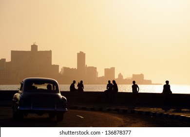 Skyline in La Habana, Cuba, at sunset, with vintage cars on the street and people sitting on the Malecon. Copy space