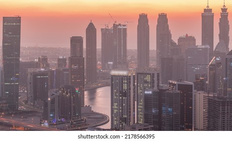 Skyline With Modern Architecture Of Dubai Business Bay Towers Day To Night Transition Timelapse. Aerial View With Canal And Construction Site After Sunset With Colorful Sky