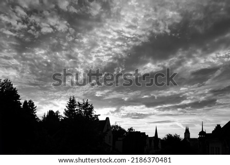Skyline of old town of Iserlohn Sauerland Germany at evening dusk with cloudy sky. Silhouettes of churches, town houses and trees after sunset. High contrast panoramic view black and white greyscale.