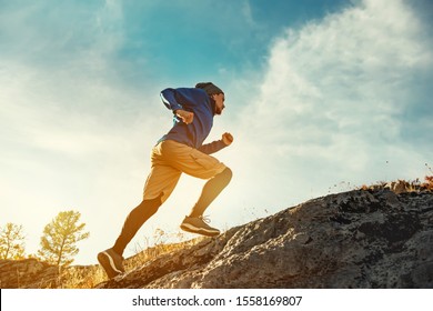 Skyrunner athlete runs uphill against sunset or sunrise sky and sun. Skyrunning concept