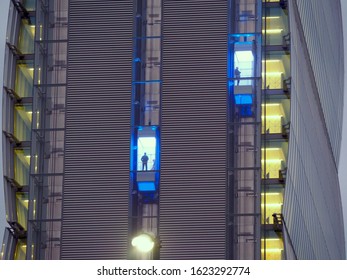 Skyscraper external elevator with unrecognizable persons silhouette inside going to work at early morning