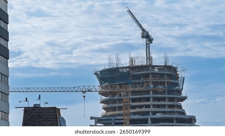 Skyscraper under construction with tower cranes and visible curved structure. Urban scene of modern architectural development.