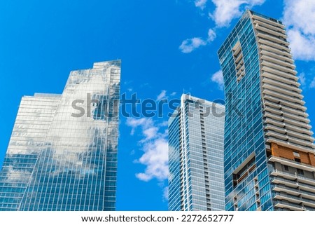 Skyscrapers camouflaged to the sky in Miami, Florida. Three modern high-rise glass buildings with sky facade left and back on right and curved structure front to the right.