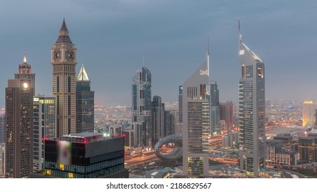 Skyscrapers On Sheikh Zayed Road And DIFC Day To Night Transition Timelapse In Dubai, UAE. Towers In Financial Centre Aerial View From Above. Cloudy Sky After Sunset