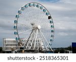 Skywheel ferris wheel with blue gondolas is rotating in front of a cloudy sky on a waterfront. Helsinki port Finland