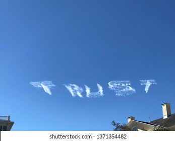 Skywriting the word trust against a perfect blue sky in summer.  The skywriting is starting to fade.  No clouds at all