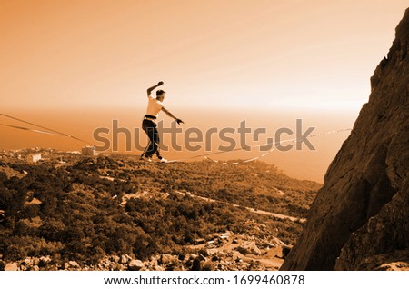 Slacklining. Man highlining on a slope at a height near a cliff overlooking the sea coast background.