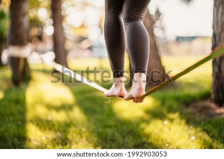 Slacklining is a practice in balance that typically uses nylon or polyester webbing. Girl walking on a slackline in a park during a sunset. Slack line