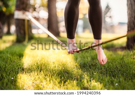 Slacklining is a practice in balance that typically uses nylon or polyester webbing. Girl walking on a slackline in a park during a sunset. Slack line