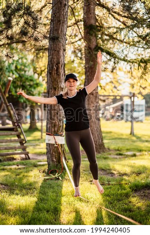 Slacklining is a practice in balance that typically uses nylon or polyester webbing. Girl walking on a slackline in a park during a sunset. Slack line