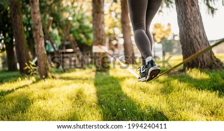 Slacklining is a practice in balance that typically uses nylon or polyester webbing. Girl walking on a slackline in a park during a sunset. Slack line